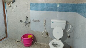 Een badkamer met een toilet, een douche en een roze emmer.