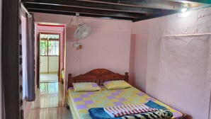 Een slaapkamer met een houten bed, een sprei, een ventilator en een deur naar een andere kamer.
