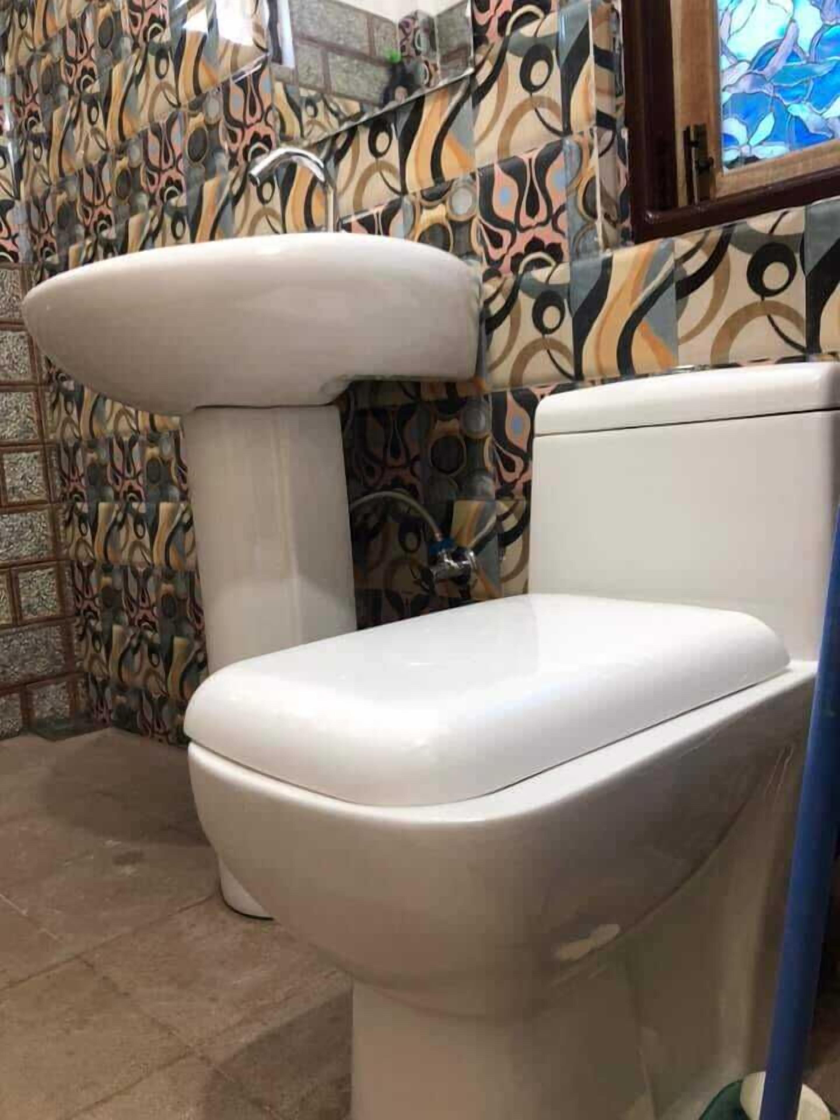 Un bagno con il water bianco, piastrelle decorate sulle pareti e una finestra con un motivo a vetrata colorata.