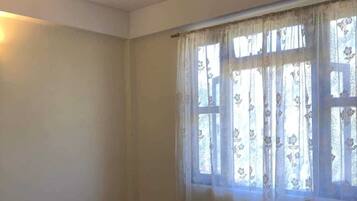 Quarto com uma cama de solteiro, cortinas florais e janela com vista.