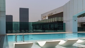 Una piscina interior moderna con paredes de vidrio transparente, sillones de descanso blancos y vistas a edificios de la ciudad.