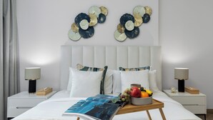 Un dormitorio moderno con una cama, dos mesitas de noche, una mesita auxiliar, una revista y un frutero.