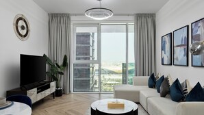 Una sala de estar moderna con un televisor de pantalla plana, una mesa redonda de centro, un sofá y un ventanal con vistas a la ciudad.