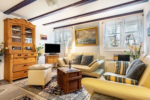 A living room with a wooden cabinet, a sofa, a television, and a painting of a ship. - Apartment 'Helgoland' with Shared Terrace, Shared Garden and Wi-Fi (Cuxhaven)