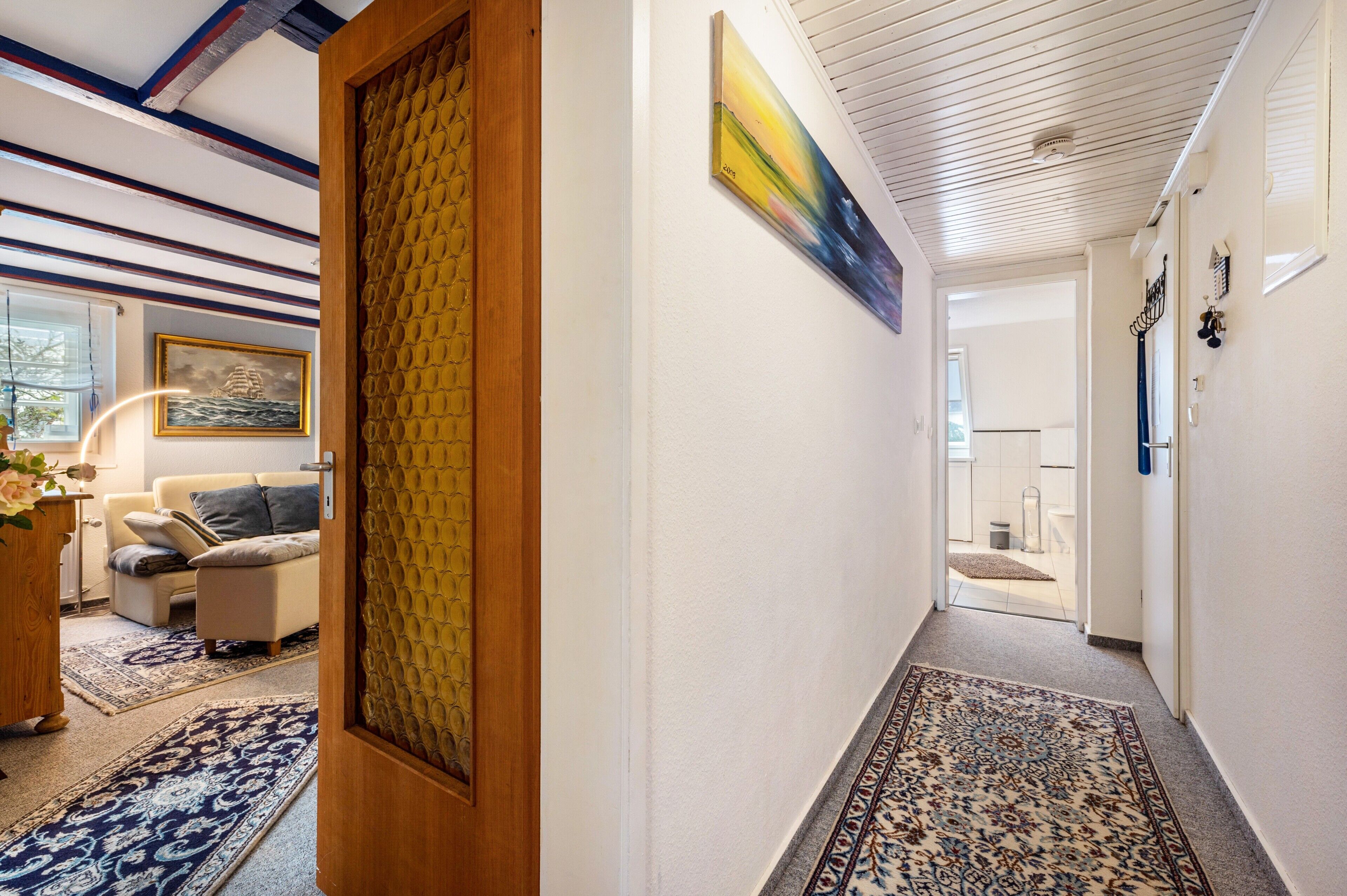 Um corredor com tapete estampado, porta de madeira e um quadro na parede.