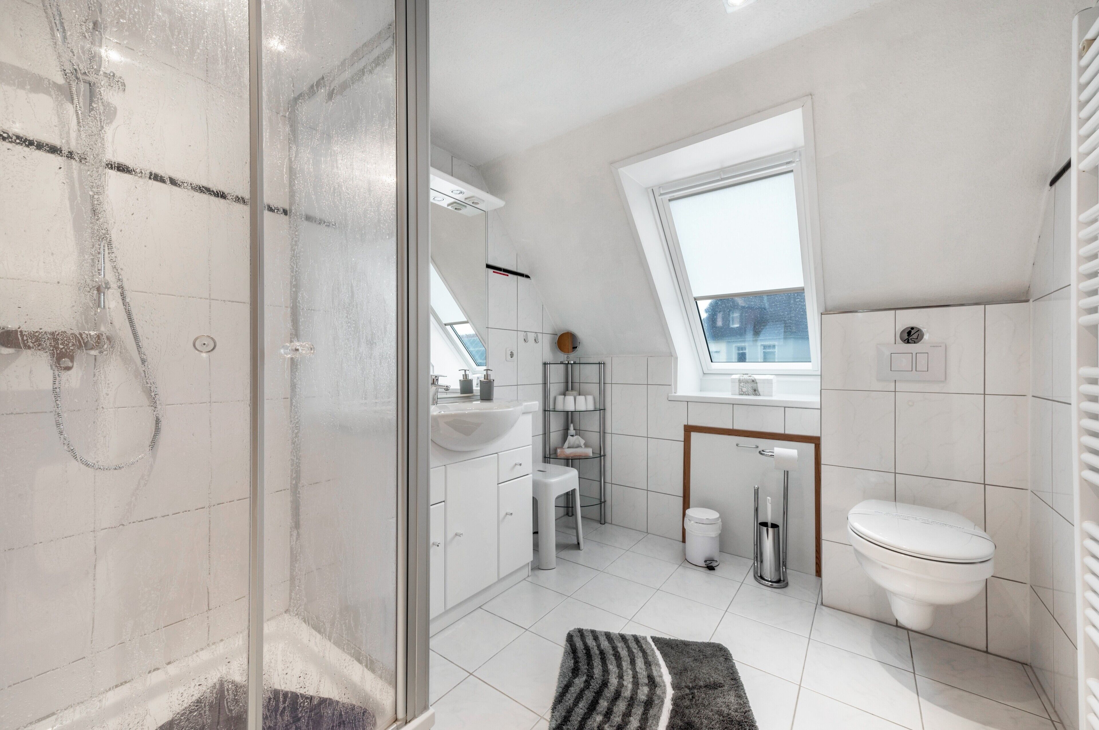 A modern bathroom with a shower, toilet, sink, and a window.