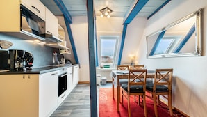 A compact kitchen with modern appliances, a dining area with a red rug, and a large mirror reflecting the room's architecture. - Apartment 'Kugelbake' with Shared Terrace, Communal Garden and Wi-Fi (Cuxhaven)