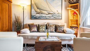 A cozy living room with a sofa, a wooden coffee table, a lamp, a bookshelf, and a painting of a sailboat. - Apartment 'Scharhörn' with Shared Terrace, Shared Garden and Wi-Fi (Cuxhaven)