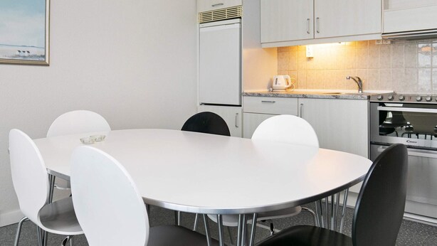 A modern kitchen with white cabinets, a white table, and black chairs. - 4 Person Holiday Park Home in Blokhus (Blokhus)