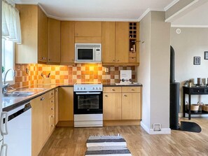A compact kitchen with wooden cabinets, a microwave, a stove, and a tiled backsplash. - 4 Star Holiday Home in Kopingsvik (Kopingsvik)