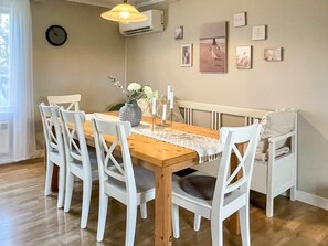 A dining area with a wooden table, white chairs, a vase with flowers, and wall-mounted pictures. - 4 Star Holiday Home in Kopingsvik (Kopingsvik)