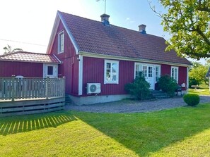 A red house with a sloped roof, a wooden deck, and a well-maintained lawn.