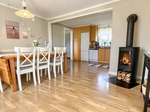 A modern kitchen with wooden cabinets, a dining area with white chairs, and a wood-burning stove.