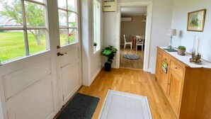 Ein Zimmer mit Holzboden, einer weißen Tür, einem Fenster, einer Pflanze, einem Schreibtisch und einem Schrank.