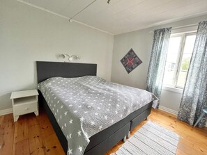 A bedroom with a bed, a nightstand, a window with curtains, and a wall-mounted light fixture.