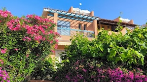 A building with a balcony, surrounded by lush greenery and flowering plants. - Sophia Bay Home - a treasure box in Peyia (Pegeia)