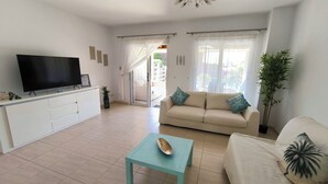 A living room with a sofa, a coffee table, a TV, and a sliding glass door leading to a balcony. - Sophia Bay Home - a treasure box in Peyia (Pegeia)