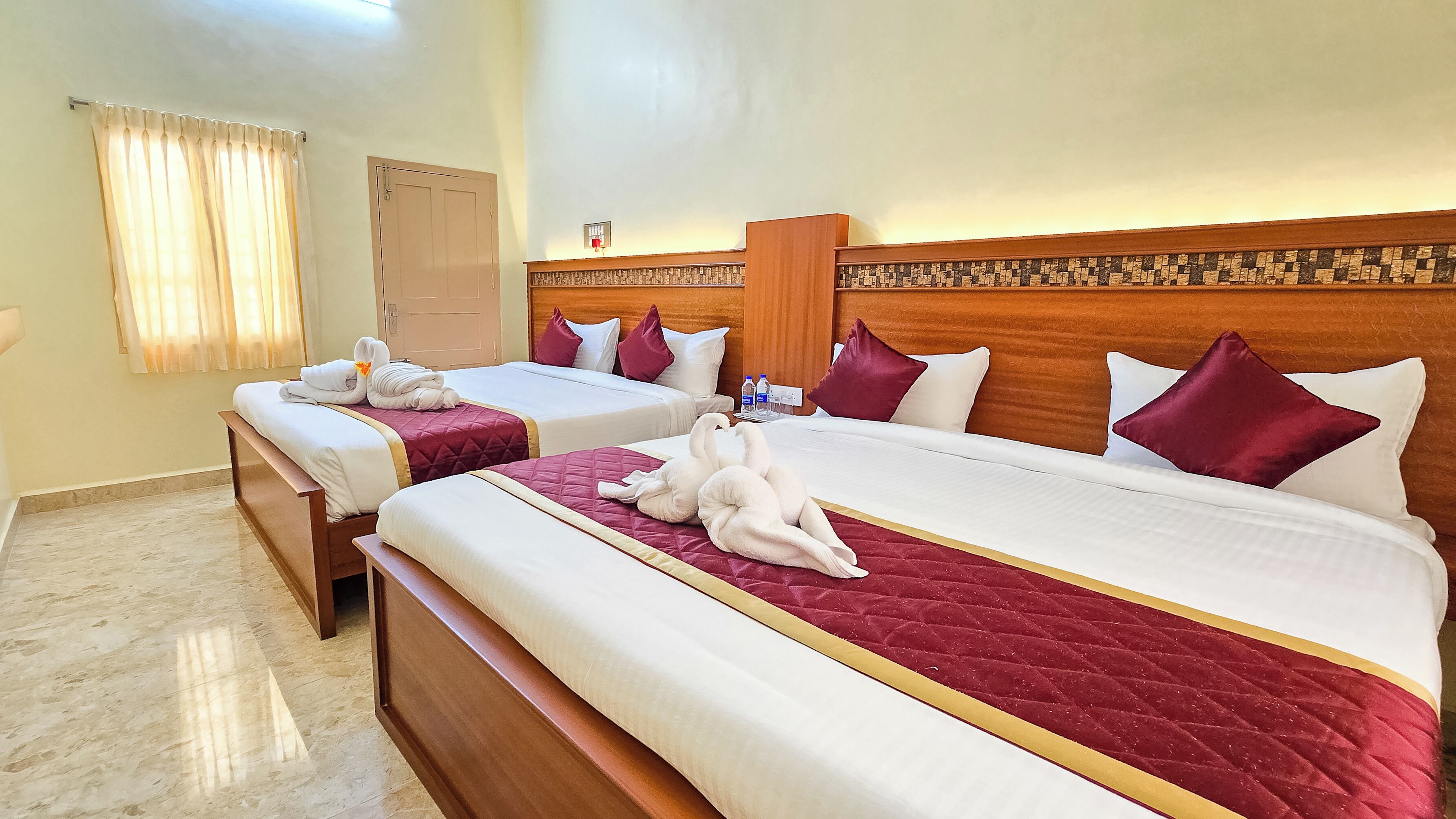 Habitación de hotel con dos camas, cada una con colcha roja y ropa de cama blanca. Hay toallas y almohadas en las camas, y un cabecero de madera con un diseño estampado.