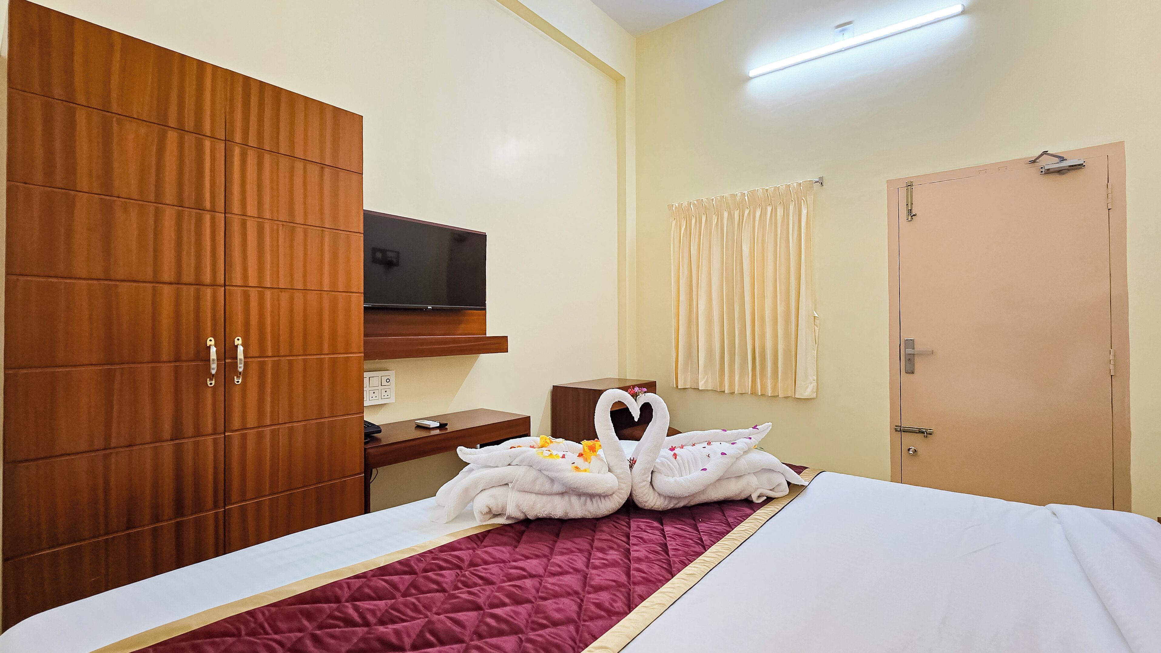 A hotel room with a bed, a wooden wardrobe, a television, a bedside table, and a door.