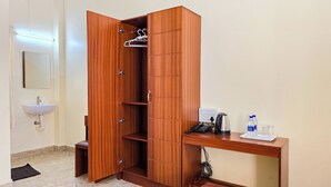 A wooden wardrobe with multiple compartments, a small bench, a sink, and a desk with a kettle, water bottles, and a phone. - Luna Castle (Palayankottai)