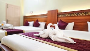 Ein Hotelzimmer mit zwei Betten, jedes mit einer violetten Tagesdecke und weißen Kissen. Auf den Betten liegen zwei weiße Handtücher in Schwanenform.