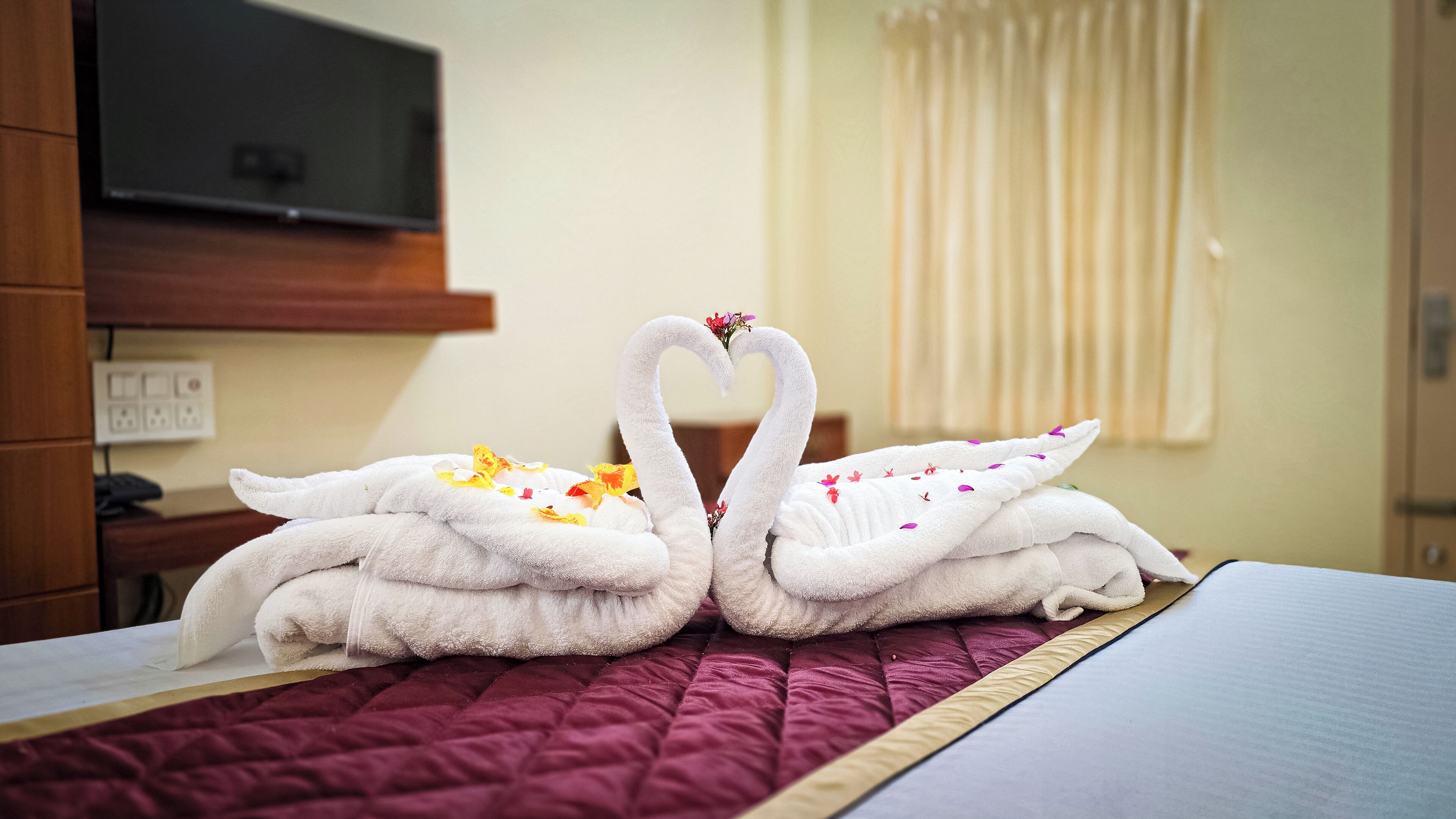 A bed with a red quilt and two towels shaped like swans with flowers.