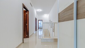 A modern hallway with a polished floor, a wooden door on the left, and a staircase with a white railing. - Villa with Jacuzzi and Beach Access, Near Diving, Paddle Boating and Camping Spots by Deluxe Holiday Homes (Fujairah)