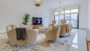 A modern living room with a large TV, comfortable seating, and a large window. - Villa with Jacuzzi and Beach Access, Near Diving, Paddle Boating and Camping Spots by Deluxe Holiday Homes (Fujairah)