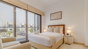 A modern bedroom with a large window, a bed with a wooden headboard, a bedside table with a lamp, and a chair. - Villa with Jacuzzi and Beach Access, Near Diving, Paddle Boating and Camping Spots by Deluxe Holiday Homes (Fujairah)