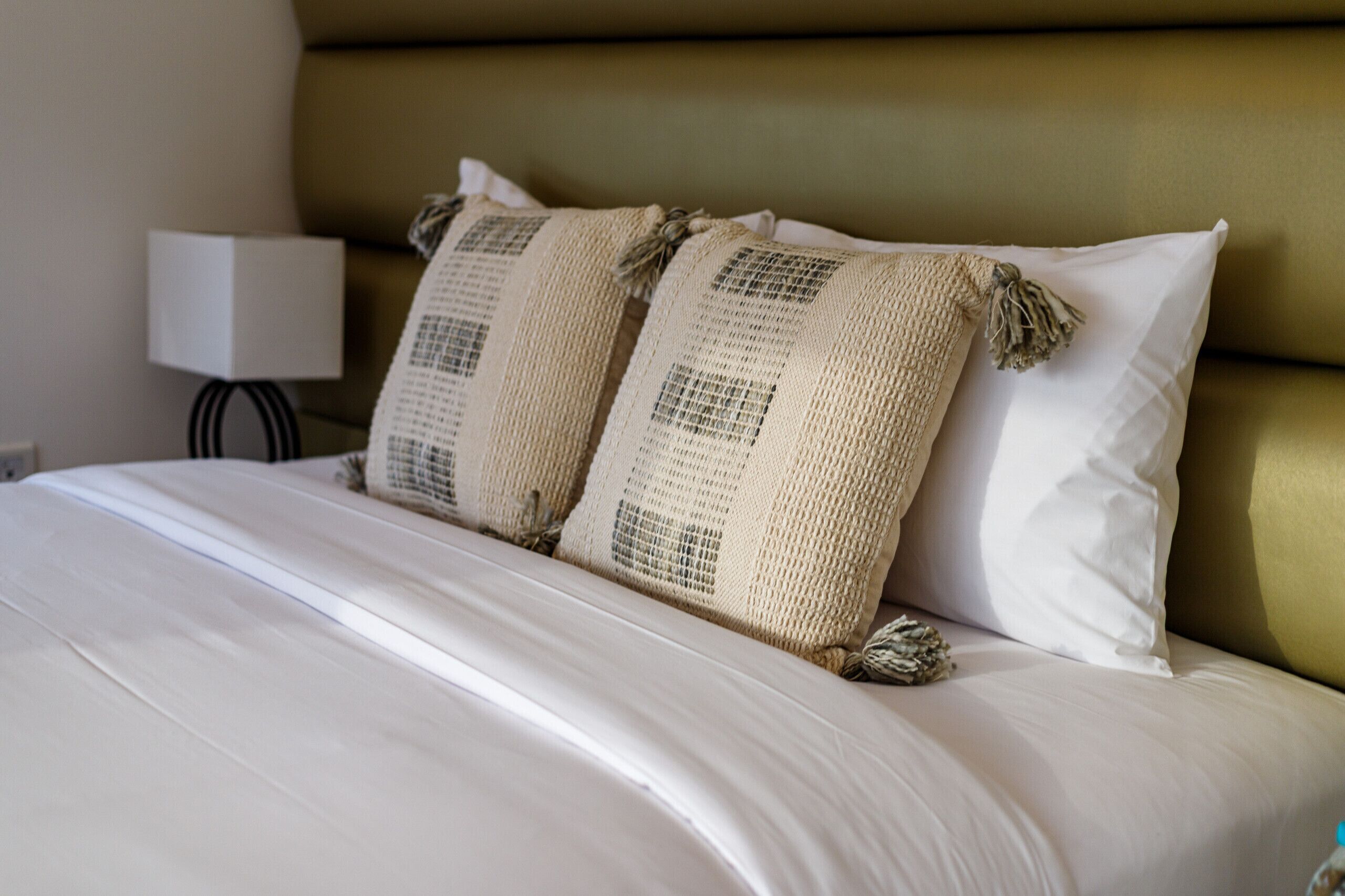Una cama bien hecha con sábanas blancas y dos almohadones con borlas.