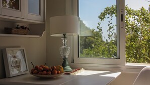 Una habitación con una mesa, un frutero, una lámpara y una ventana con vistas a la vegetación.