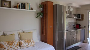 Un dormitorio con cama, almohadas, una mesita de noche y un estante con libros y una planta.