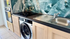A modern kitchen with a built-in washing machine, a stainless steel sink, and a marble backsplash.