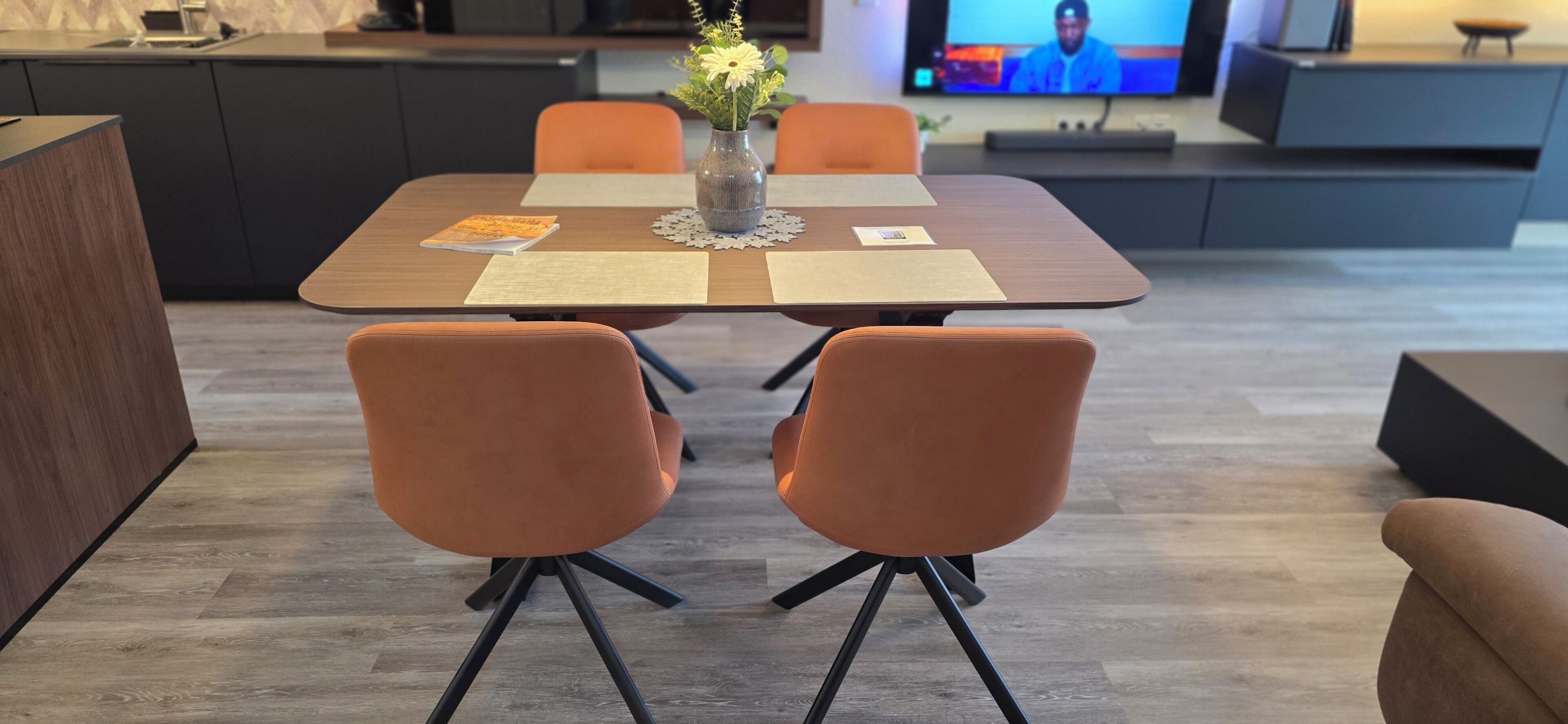 A modern dining area with a wooden table, two orange chairs, and a vase with flowers.