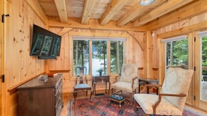 Ein Holzblockhaus-Interieur mit einem großen Fenster, zwei Stühlen, einem kleinen Tisch und einem Schrank.