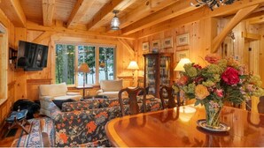 Ein Holzhütten-Innenraum mit Esstisch, Stühlen, einer Couch und einem an der Wand befestigten Fernseher.