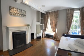 A bedroom with a fireplace, a bed with white linens, and a large window with curtains. - Covent Garden House, 4-bed, Sleeps 10 (London)