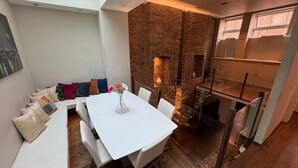 A dining area with a white table and chairs, a brick wall, and a seating area with cushions.