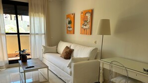 Un salon moderne avec un canapé blanc, une table basse, un bureau en verre transparent et une lampe.