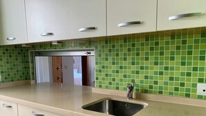 Une cuisine équipée d’un évier, de placards et d’un plan de travail recouvert de carreaux verts.