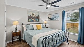 A bedroom with a bed, two bedside tables, a ceiling fan, and a window with curtains.
