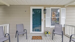 A porch with two chairs, a welcome mat, and a potted plant.