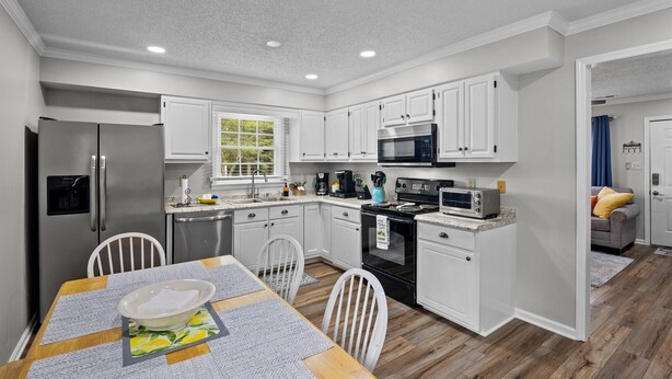 A modern kitchen with white cabinets, stainless steel appliances, and a dining area with a table and chairs.