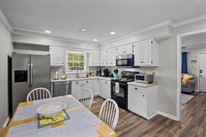 A modern kitchen with white cabinets, stainless steel appliances, and a dining area with a table and chairs. - 3BR Retreat with King Suite and Pet-Friendly with Fully Fenced Yard (New Bern)