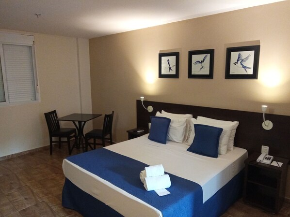A hotel room with a bed, bedside table, nightstand, and a desk with chairs. There are framed pictures on the wall.