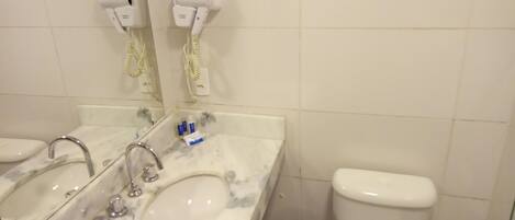 A bathroom with a marble sink, two faucets, a mirror, a toilet, and two hair dryers mounted on the wall.