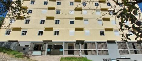 Un edificio de varios pisos con fachada amarilla, múltiples balcones y una entrada a nivel de calle con puertas de vidrio.