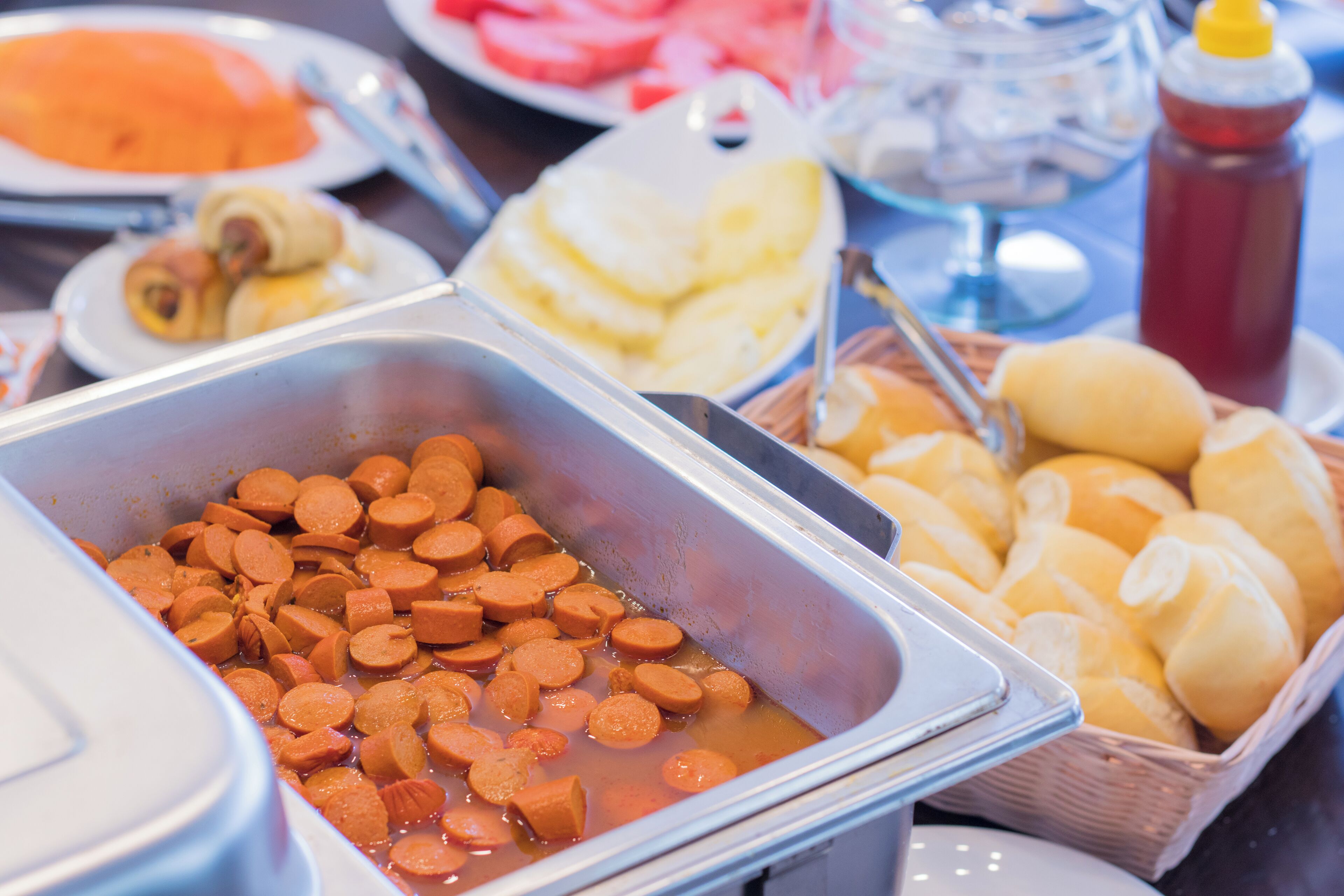 Un bufé con diversos alimentos, incluyendo salchichas en rodajas, panes y un recipiente de sopa.