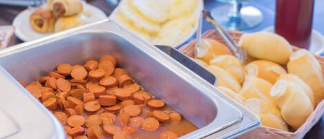 Un bufé con diversos alimentos, incluyendo salchichas en rodajas, panes y un recipiente de sopa.