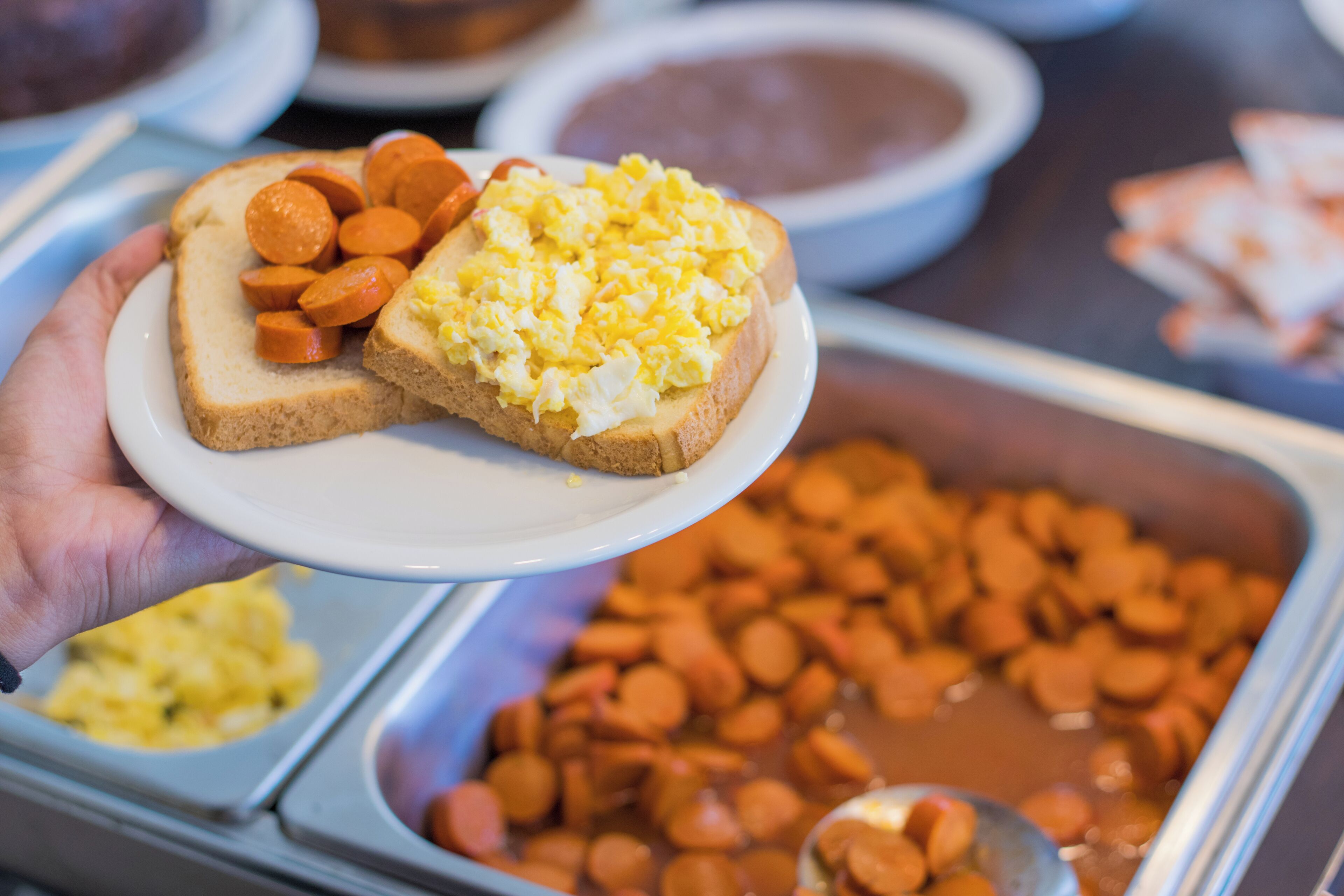 A buffet with various food items including sliced sausages, scrambled eggs, and a plate with toast and carrots.